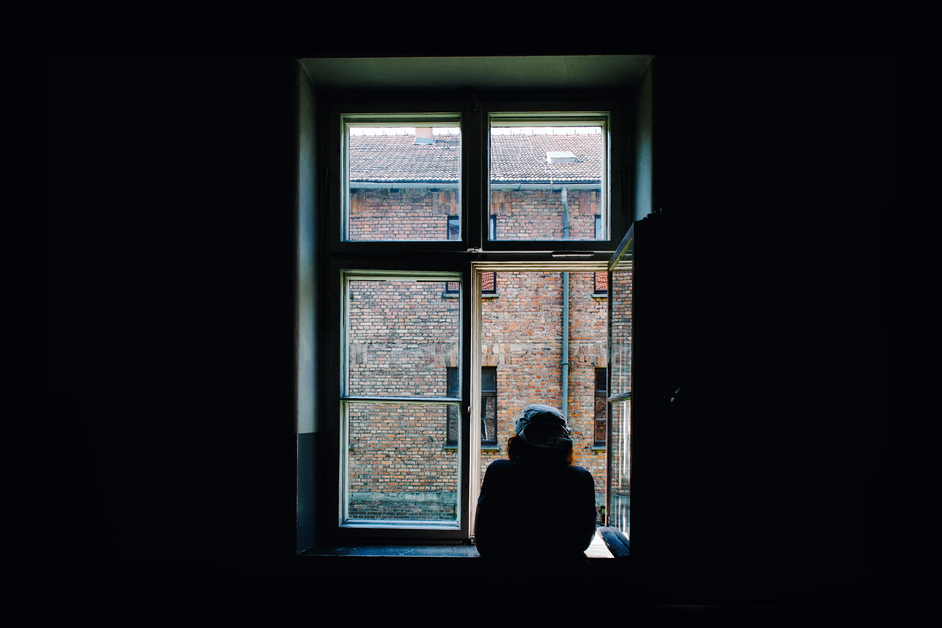A person looking through the window of his dark room