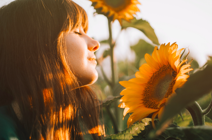 eine junge Frau, die das Sonnenlicht neben einer Sonnenblume genießt