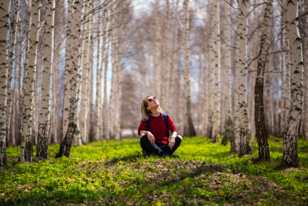Frau sitzt zwischen braunen Bäumen und genießt die Sonne