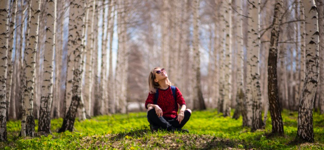 Frau sitzt zwischen braunen Bäumen und genießt die Sonne