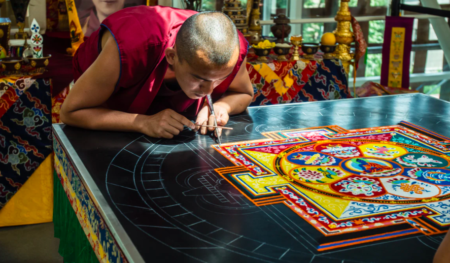 Ein tibetischer Mönch macht ein Mandala aus farbigem Sand