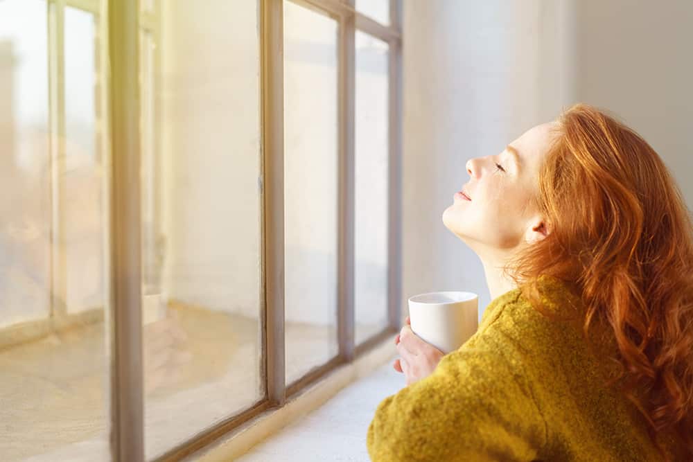 Eine junge Frau genießt die Wärme der Sonne durch ihr Fenster