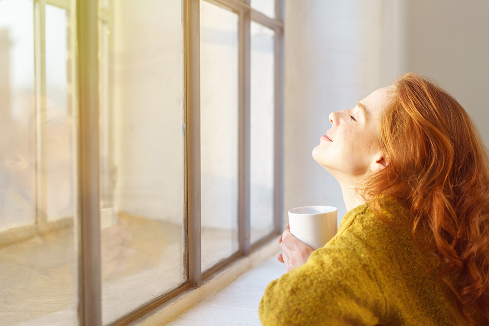 A young woman enjoying the warmth of the sun through her window