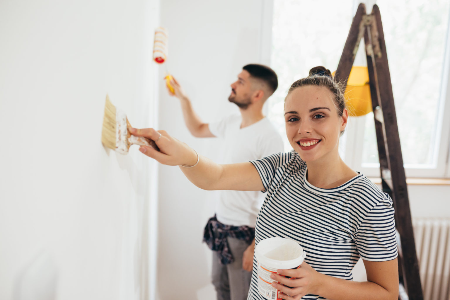 a young couple painting their wall in white