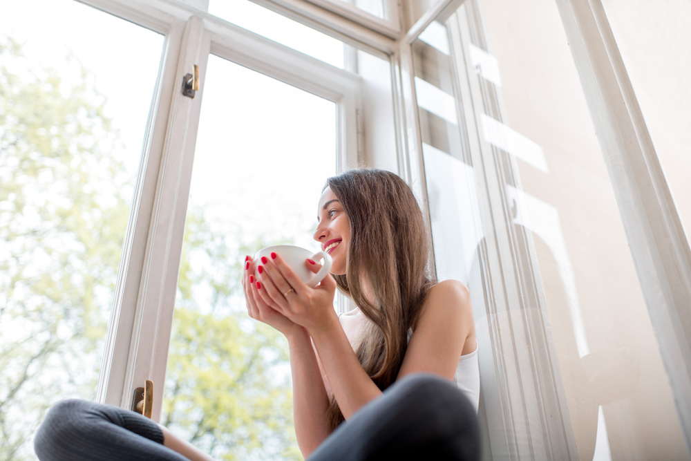 A young woman sitting in front of her window, enjoying the natural light
