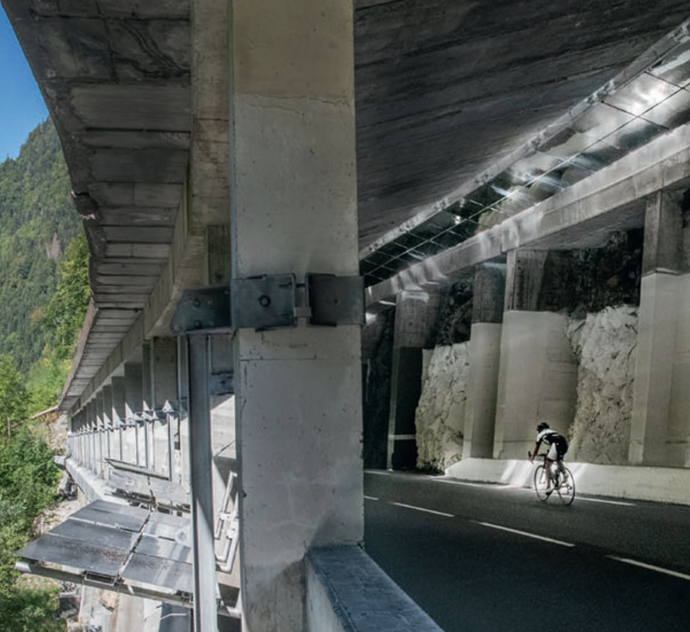 Un cycliste sportif dévale la route de montagne. Il passe sous une galerie paravalanche illuminée par des Réflecteurs d'éclairage naturel